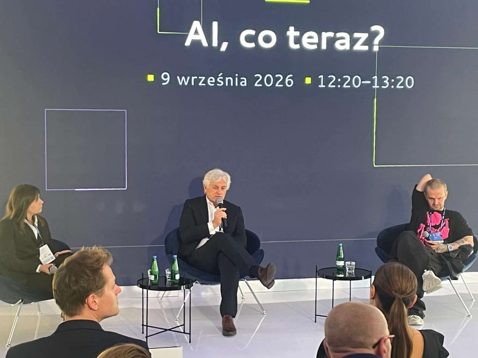 Panel zatytułowany „AI, co teraz?” 9 września 2026, na scenie troje uczestników, mówi mężczyzna siedzący pośrodku.